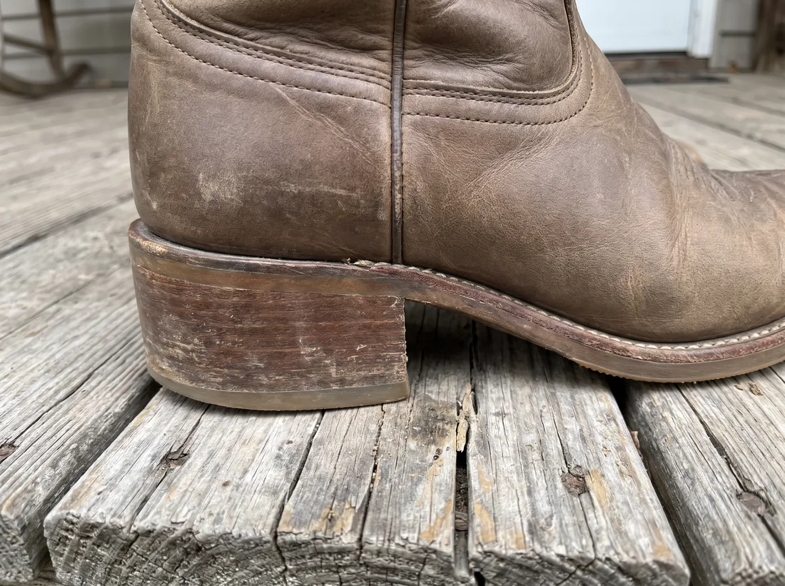 The heel of a worn brown leather western boot, showing layers of stacked leather and welt stitching.